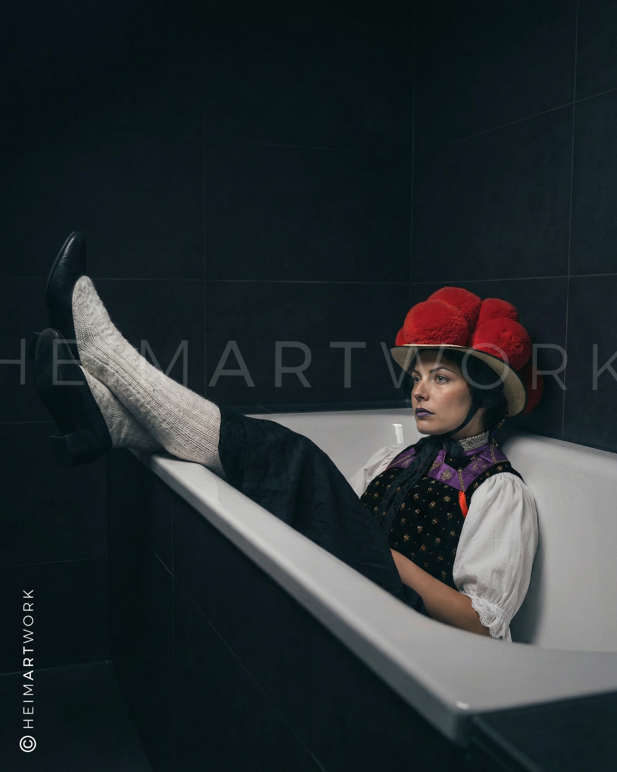 Künstlerisches Porträt einer Frau in traditioneller Schwarzwälder Tracht inklusive rotem Bollenhut und Wollsocken, die in einer weißen Badewanne vor einem dunklen, gefliesten Hintergrund posiert.