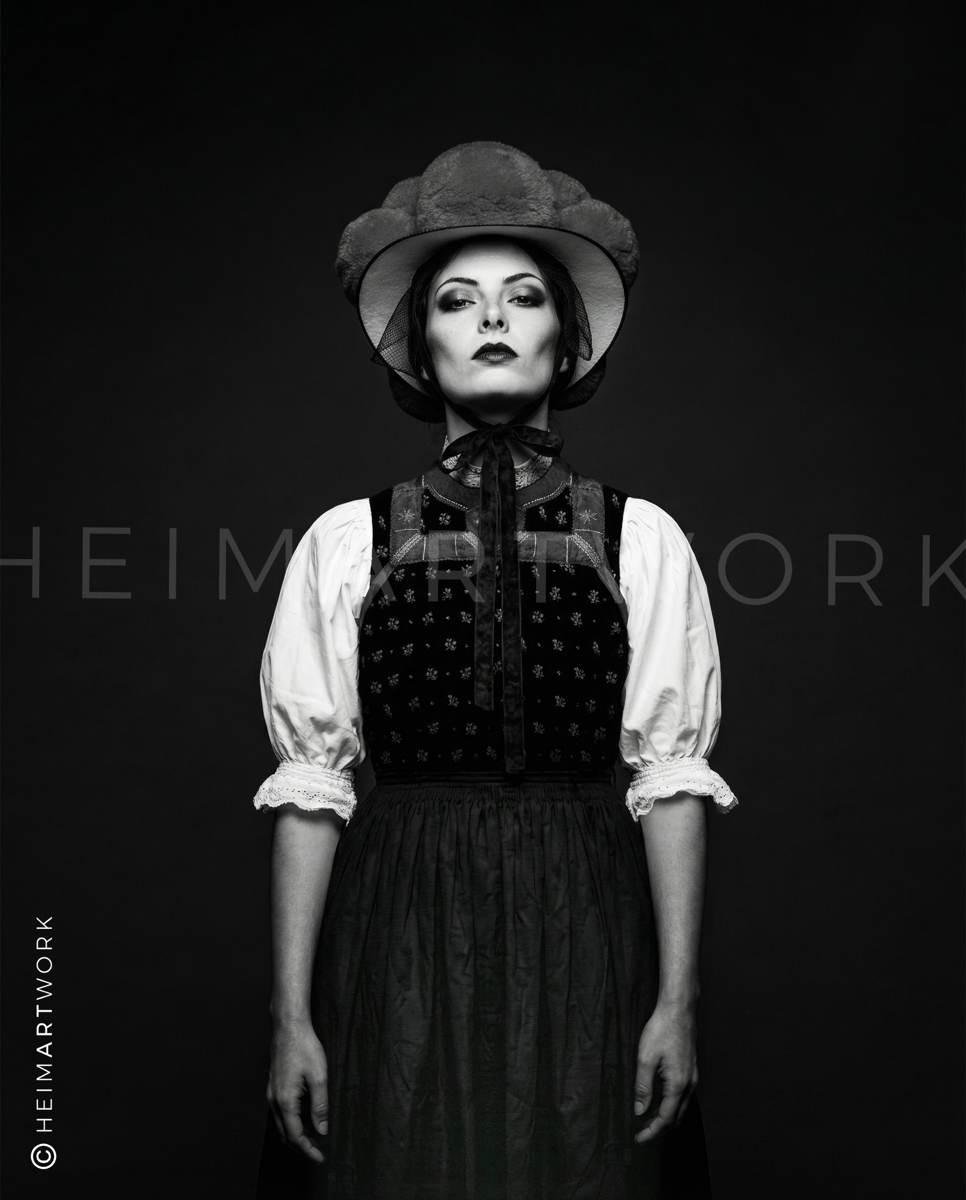 Künstlerische Schwarz-Weiß-Fotografie einer Schwarzwälderin in traditionellem Mieder und Bollenhut. Diese Schwarzwald Leinwand fängt die feinen Details der Stickerei und den entschlossenen Blick der Porträtierten in edler Monochrom-Optik ein.