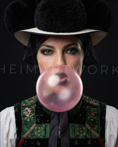 Detailreiches Porträt einer Frau in traditioneller Schwarzwälder Tracht mit schwarzem Bollenhut, die eine große rosa Kaugummiblase bläst, vor einem tiefdunklen Hintergrund.