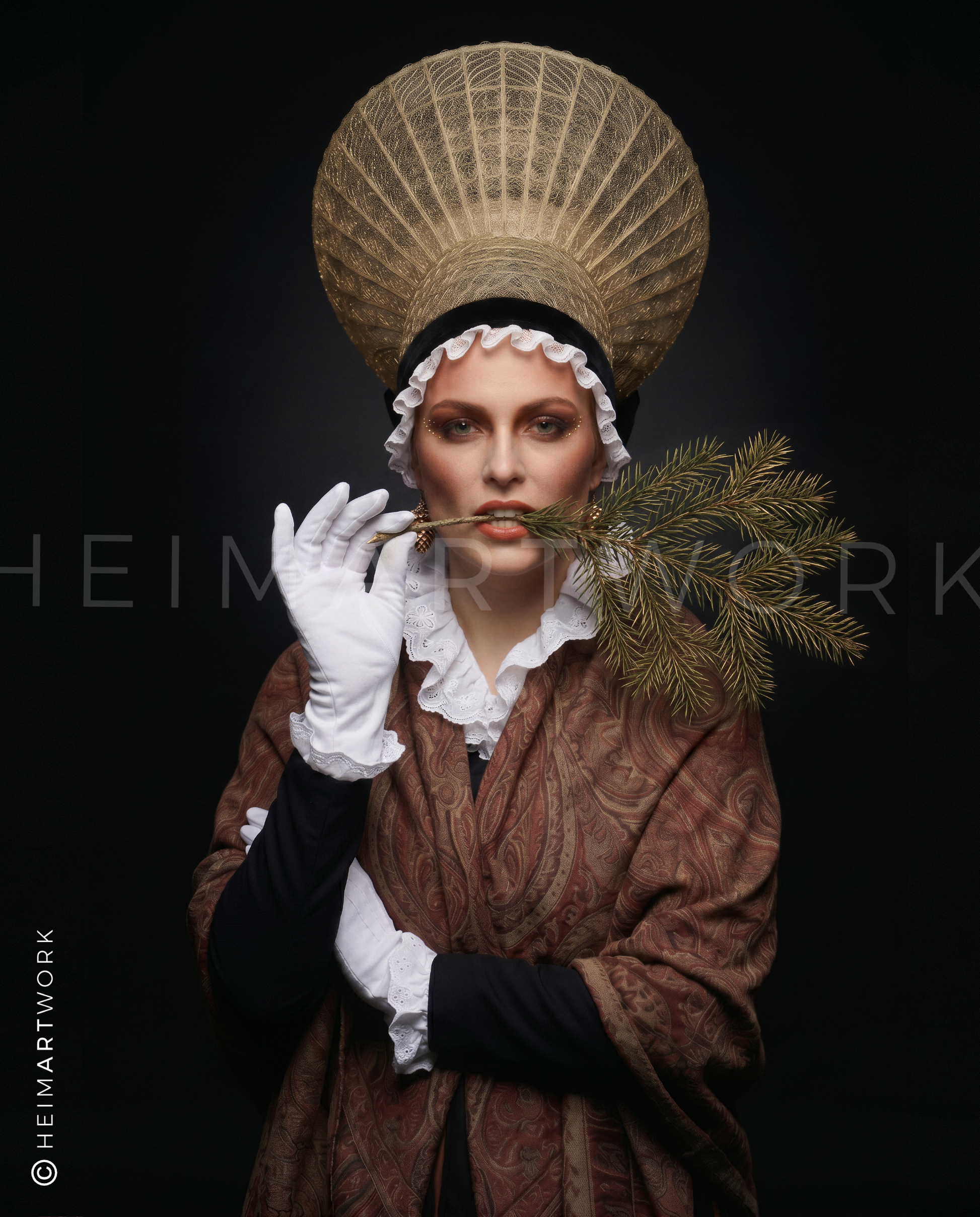 Das Motiv zeigt das hochwertige Porträt einer jungen Frau in der detailgetreuen, traditionellen Schwarzwälder Tracht inklusive goldener Radhaube und weißen Handschuhen. Sie blickt vor einem dunklen Hintergrund elegant in die Kamera und hält einen echten Tannenzweig im Mund.