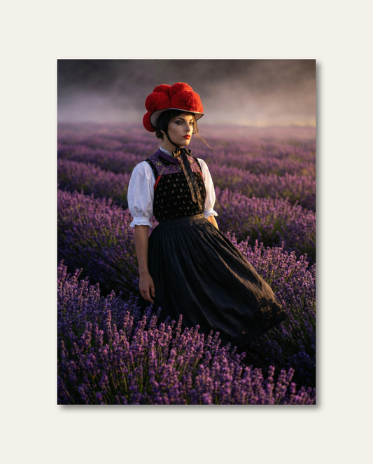Hochwertige Schwarzwald Leinwand – kunstvolle Bollenhut-Interpretation voller Eleganz, warmer Lichtstimmung und ländlicher Magie.  Eine Frau in traditioneller Schwarzwälder Tracht mit leuchtend rotem Bollenhut steht inmitten eines blühenden, violetten Lavendelfeldes. Das warme Abendlicht verleiht der surrealen Symbiose aus Schwarzwälder Heimat-Tradition und romantischer Naturkulisse eine traumhafte Ästhetik.