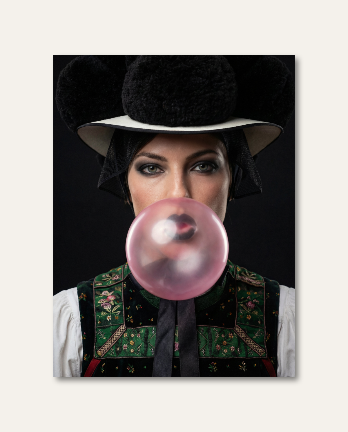 Eine Frau in klassischer Schwarzwälder Tracht mit schwarzem Bollenhut pustet eine große, rosa Kaugummiblase vor einem dunklen Studiohintergrund. Die humorvolle Kombination aus traditionellem Heimatmotiv und frecher Pop-Art-Ästhetik schafft ein modernes, ausdrucksstarkes Kunstwerk.