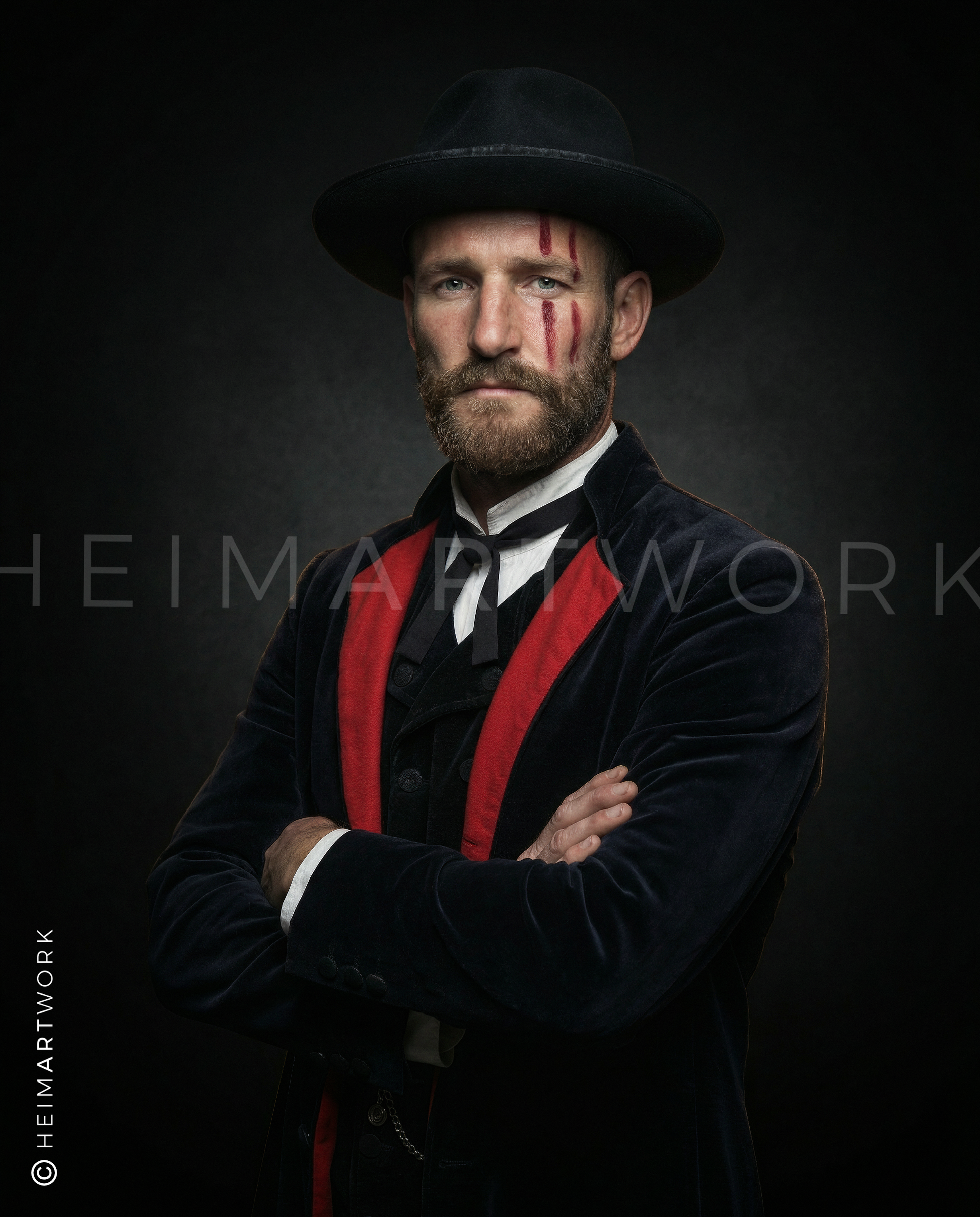 Das Motiv zeigt ein markantes Porträt eines Mannes in traditionell inspirierter Schwarzwälder Tracht mit dunklem Hut und Samtjacke mit roten Akzenten. Sein Gesicht ist von drei roten vertikalen Streifen gezeichnet, was dem Bild eine archaische und kämpferische Note verleiht. Die verschränkten Arme und der ernste Blick vor tiefschwarzem Hintergrund erzeugen eine kraftvolle, fast mystische Atmosphäre.