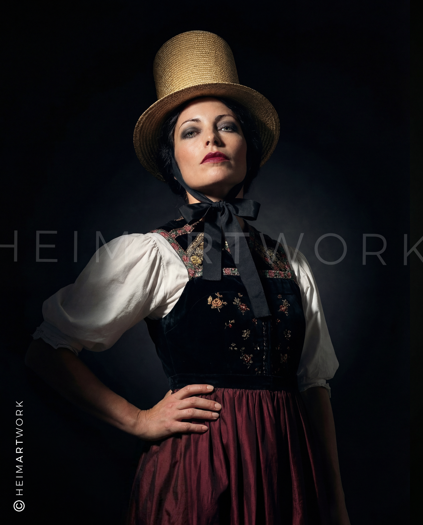 Das Motiv ist ein elegantes Porträt einer Frau in traditioneller Schwarzwälder Tracht. Sie trägt einen markanten, hohen Strohzylinder mit schwarzer Schluppe (Kappe) und ein besticktes Samtmieder über einer weißen Bluse mit Puffärmeln. Der dunkle, fast schwarze Hintergrund betont die Texturen und die tiefe Farbgebung der Tracht.