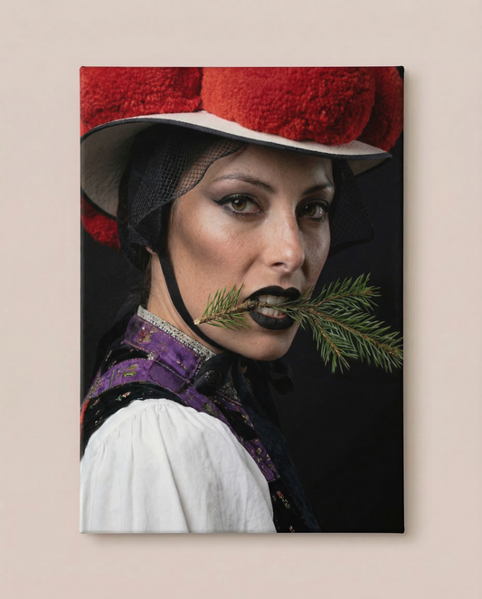 Frontalansicht an einer hellen Wand: Dieses markante Schwarzwald Wandbild zeigt eine Nahaufnahme einer Frau in violetter Tracht mit rotem Bollenhut, die einen Tannenzweig zwischen den Zähnen hält.