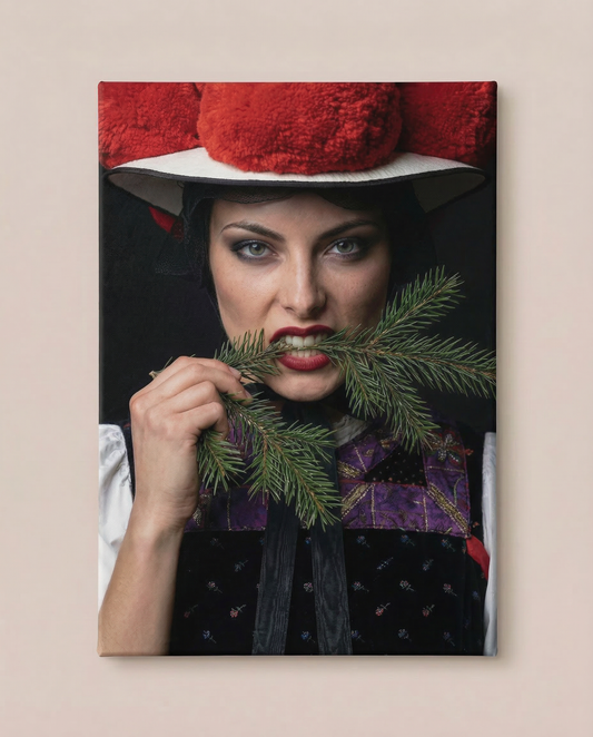 Frontalansicht an einer hellen Wand: Dieser ausdrucksstarke Schwarzwald Bild auf Leinwand zeigt eine Nahaufnahme einer Frau in violetter Tracht mit rotem Bollenhut, die entschlossen in einen Tannenzweig beißt.